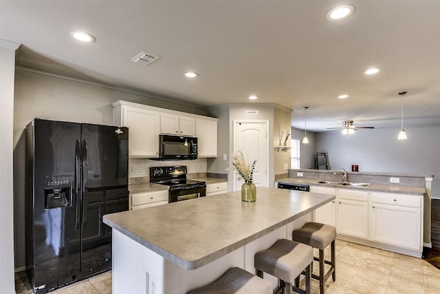 kitchen featuring sink, a breakfast bar, hanging light fixtures, black appliances, and a kitchen island