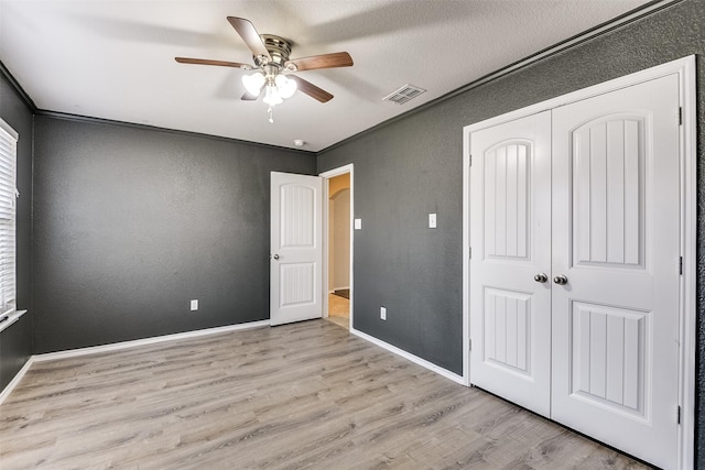 unfurnished bedroom featuring ornamental molding, a closet, ceiling fan, and light wood-type flooring