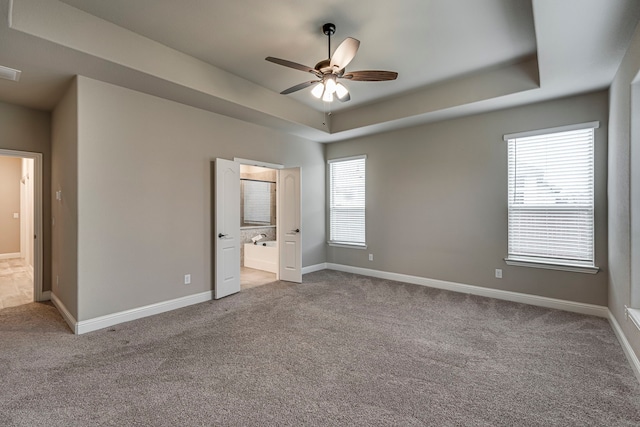 unfurnished bedroom with ceiling fan, light colored carpet, ensuite bathroom, and a tray ceiling