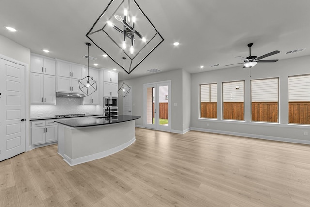 kitchen featuring under cabinet range hood, dark countertops, visible vents, stainless steel microwave, and white cabinetry