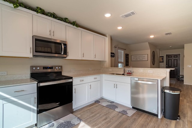 kitchen featuring light hardwood / wood-style flooring, kitchen peninsula, white cabinets, and appliances with stainless steel finishes