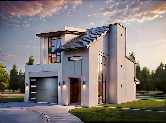 contemporary home featuring metal roof, an attached garage, driveway, stucco siding, and a front yard