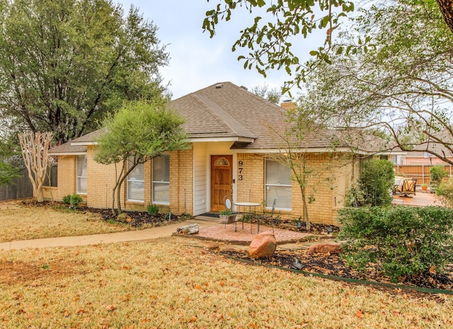 ranch-style house featuring a shingled roof, a chimney, a front lawn, a patio area, and brick siding