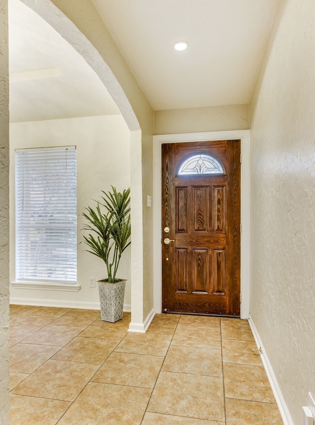 tiled foyer featuring baseboards, arched walkways, and a textured wall