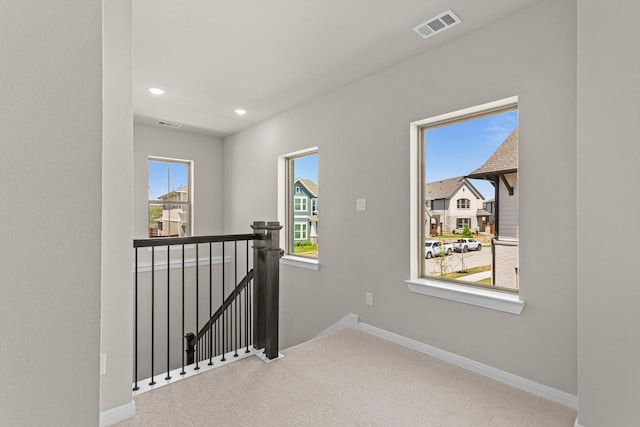 hallway with visible vents, baseboards, an upstairs landing, and carpet floors