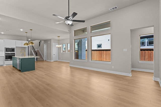 unfurnished living room with a sink, visible vents, ceiling fan with notable chandelier, and baseboards