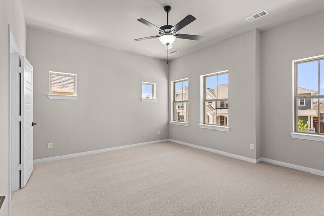 spare room with light colored carpet, ceiling fan, baseboards, and visible vents