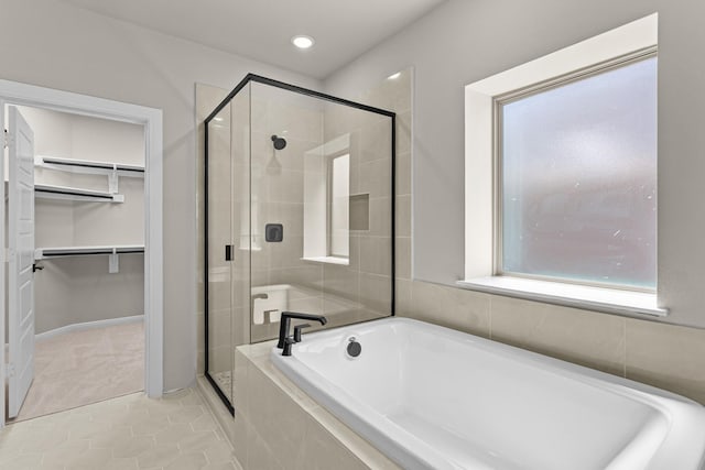 full bath with a bath, a stall shower, a spacious closet, and tile patterned flooring