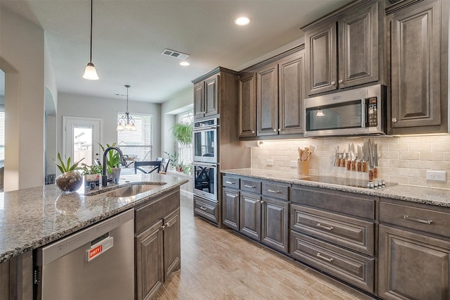 kitchen with appliances with stainless steel finishes, sink, hanging light fixtures, light stone counters, and dark brown cabinetry