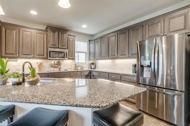 kitchen featuring appliances with stainless steel finishes, tasteful backsplash, sink, a breakfast bar area, and light stone counters