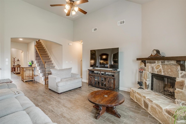 living room featuring ceiling fan, a fireplace, hardwood / wood-style floors, and a high ceiling