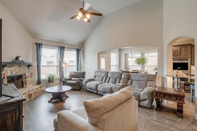 living room featuring a stone fireplace, ceiling fan with notable chandelier, high vaulted ceiling, and hardwood / wood-style flooring