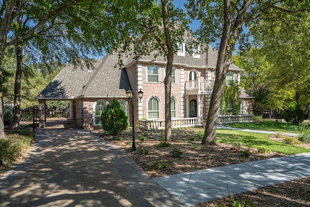 view of front of property featuring roof with shingles, a gate, fence, a balcony, and driveway