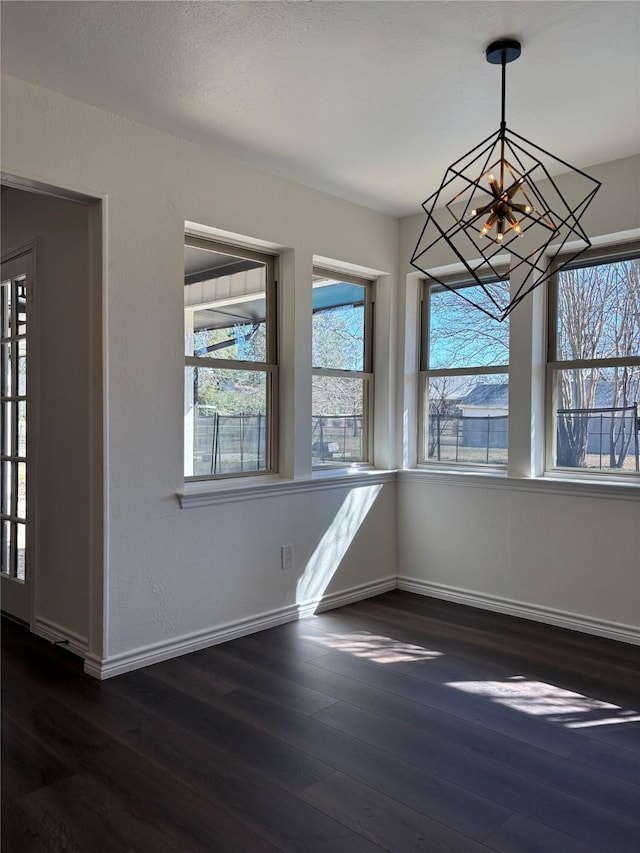 unfurnished dining area featuring baseboards, dark wood-type flooring, and a notable chandelier