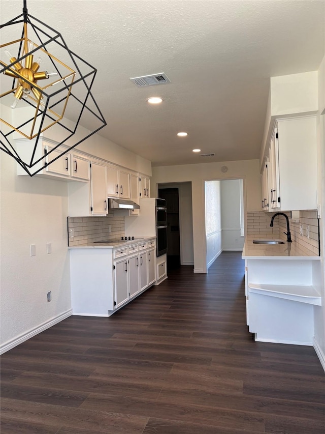 kitchen featuring light countertops, dark wood-type flooring, under cabinet range hood, and white cabinets