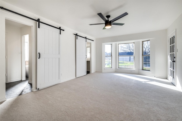 interior space featuring a ceiling fan, light carpet, ensuite bathroom, and a barn door