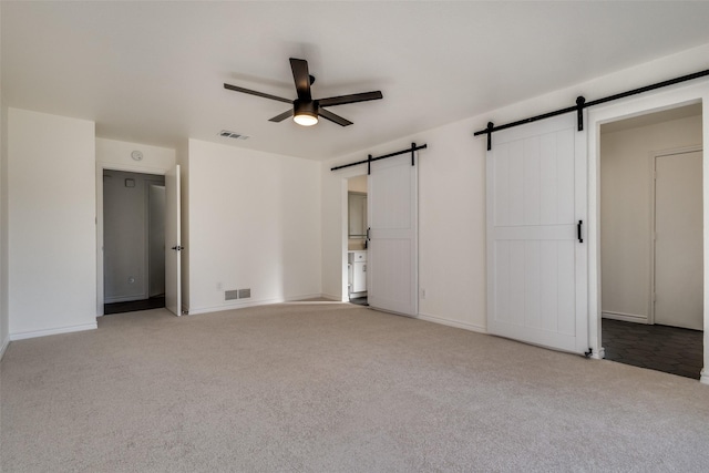 unfurnished bedroom with light carpet, a barn door, visible vents, and baseboards