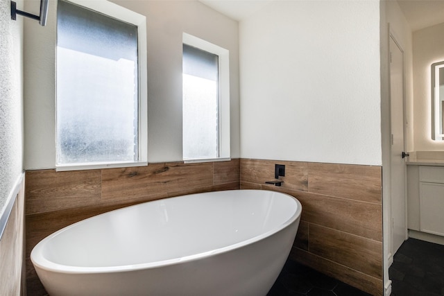 bathroom with a wainscoted wall, a freestanding tub, and tile walls