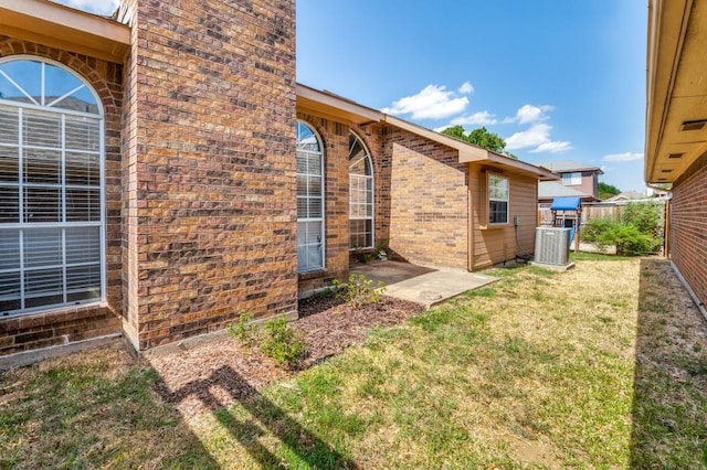 view of side of property with a yard, central AC, brick siding, and fence