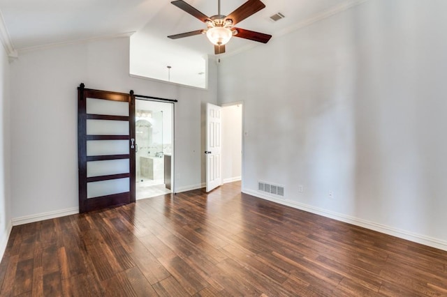 unfurnished room with dark wood-type flooring, a ceiling fan, visible vents, and a barn door