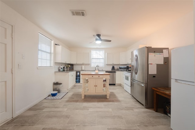 kitchen featuring a kitchen island, white cabinetry, decorative backsplash, ceiling fan, and stainless steel appliances