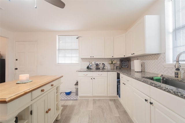 kitchen with sink, ceiling fan, white cabinets, decorative backsplash, and dark stone counters