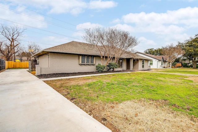 ranch-style house with brick siding, fence, concrete driveway, roof with shingles, and a front yard