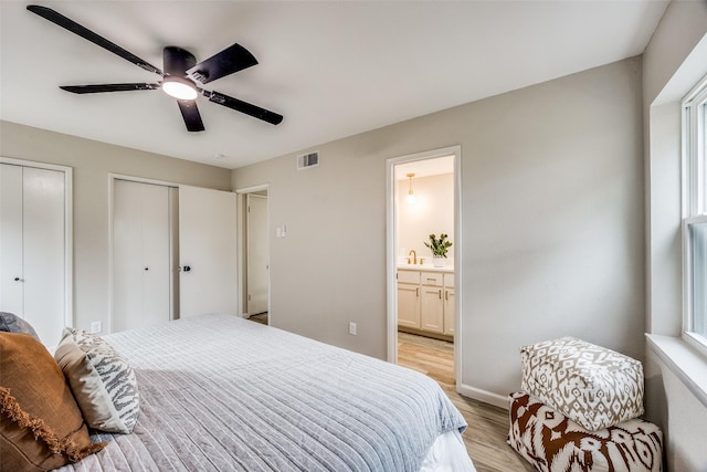 bedroom featuring ensuite bathroom, two closets, sink, ceiling fan, and light hardwood / wood-style floors