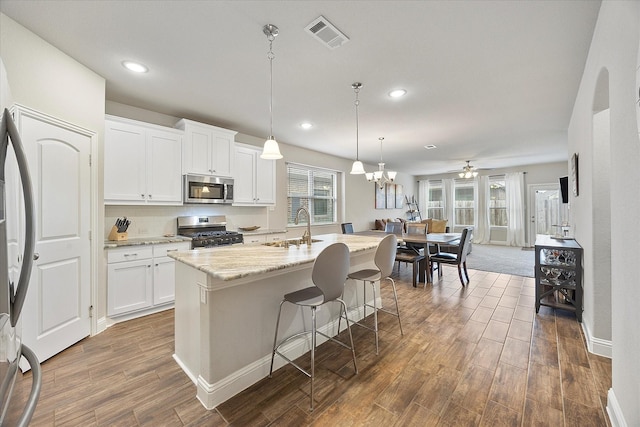 kitchen featuring white cabinetry, appliances with stainless steel finishes, an island with sink, and pendant lighting