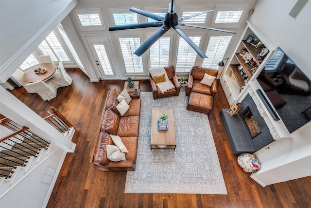 living room with ceiling fan, dark hardwood / wood-style flooring, a brick fireplace, and a towering ceiling