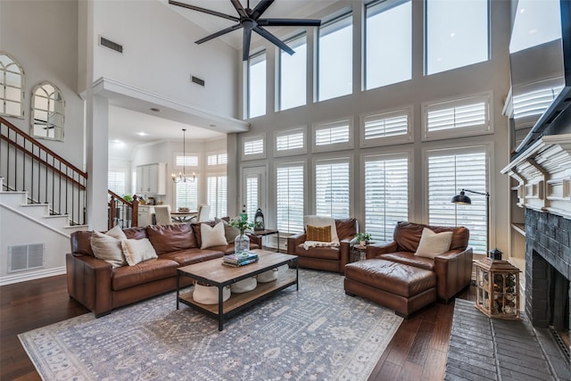 living room featuring dark hardwood / wood-style flooring, ceiling fan with notable chandelier, and a brick fireplace