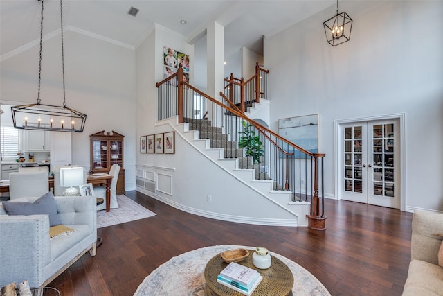 living room featuring dark wood-type flooring, french doors, an inviting chandelier, ornamental molding, and a high ceiling