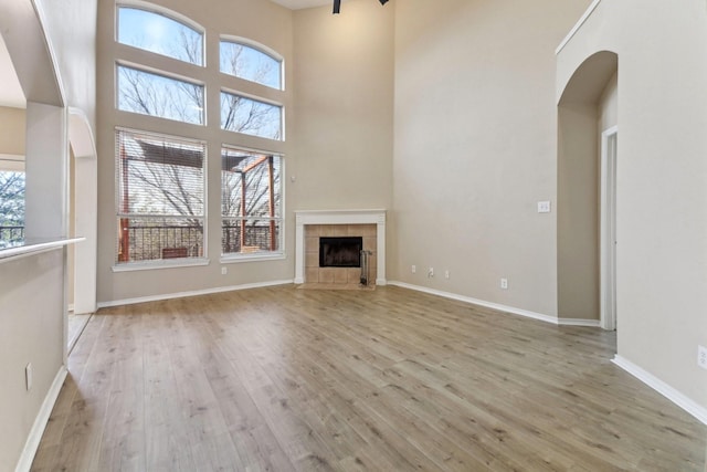 unfurnished living room with a high ceiling, a tile fireplace, and light hardwood / wood-style flooring