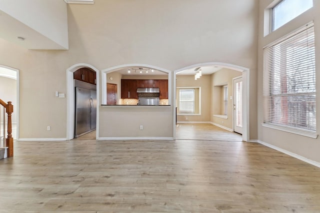 unfurnished living room with a towering ceiling, plenty of natural light, and light hardwood / wood-style flooring