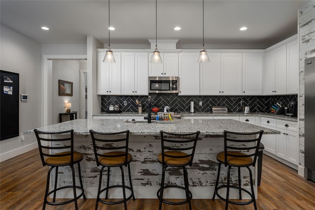 kitchen featuring white cabinetry, hanging light fixtures, a breakfast bar, and a center island with sink