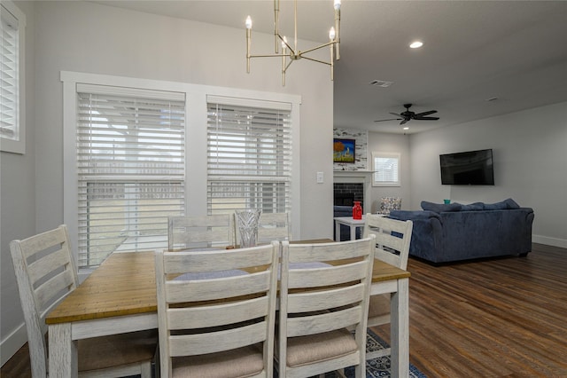 dining area featuring a large fireplace, dark hardwood / wood-style floors, and ceiling fan with notable chandelier