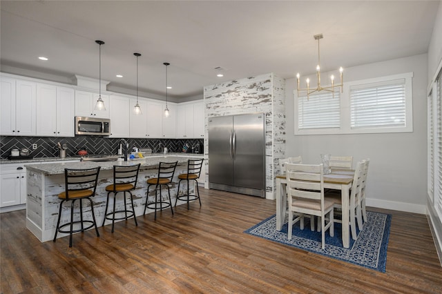 kitchen featuring white cabinetry, hanging light fixtures, a center island with sink, appliances with stainless steel finishes, and light stone countertops