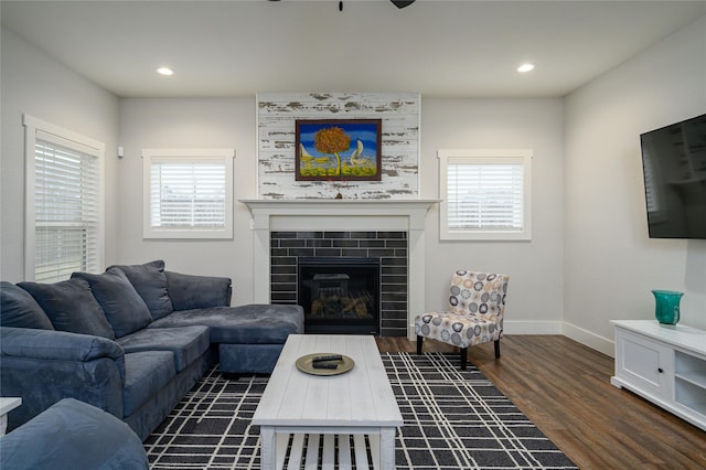 living room featuring dark wood-type flooring, a tiled fireplace, and a wealth of natural light