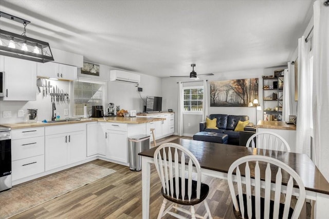 kitchen with hanging light fixtures, light wood-type flooring, a wall unit AC, ceiling fan, and white cabinets