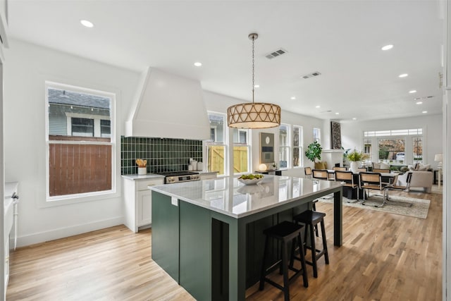 kitchen featuring white cabinetry, hanging light fixtures, custom exhaust hood, light stone countertops, and light wood-type flooring