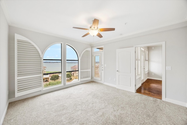 carpeted empty room featuring crown molding, ceiling fan, and a water view