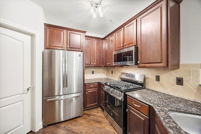 kitchen with sink, dark wood-type flooring, dark stone countertops, stainless steel appliances, and tasteful backsplash