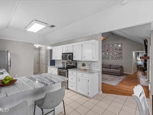 kitchen featuring stainless steel appliances, white cabinetry, vaulted ceiling, and light tile patterned floors