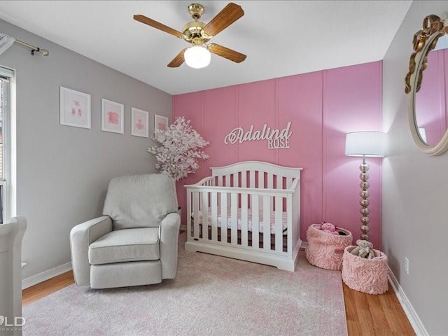 bedroom featuring a nursery area, ceiling fan, and light hardwood / wood-style flooring