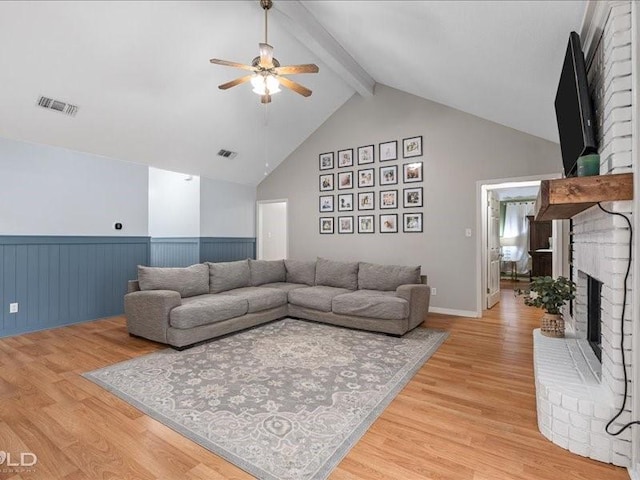 living room with high vaulted ceiling, a fireplace, light wood-type flooring, ceiling fan, and beam ceiling