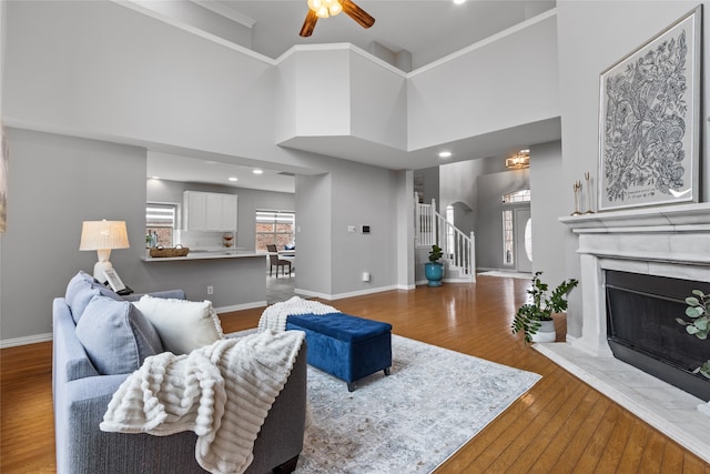 living room with ceiling fan, wood-type flooring, ornamental molding, and a high ceiling