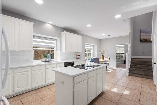 kitchen featuring sink, light tile patterned floors, tasteful backsplash, black appliances, and white cabinets