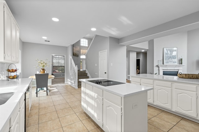 kitchen with white cabinetry, backsplash, a kitchen island, black electric stovetop, and light tile patterned flooring