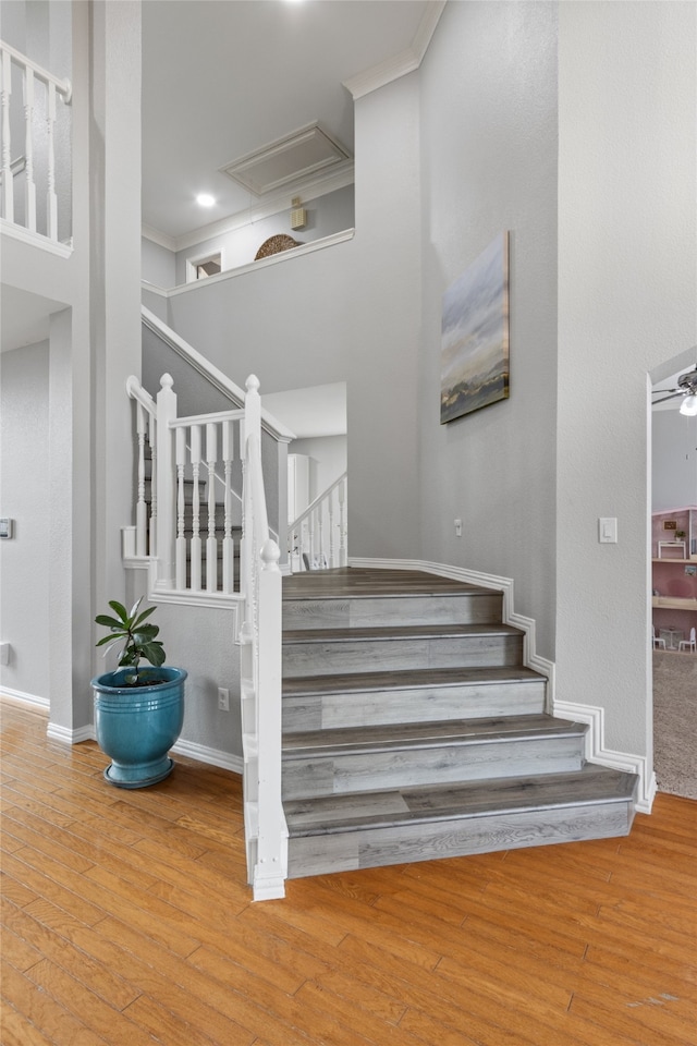 stairway featuring hardwood / wood-style flooring, crown molding, and a high ceiling