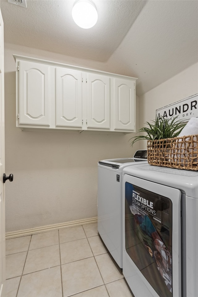 laundry area with cabinets, light tile patterned floors, a textured ceiling, and washer and clothes dryer